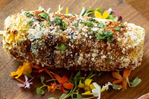 Elote grilled corn on the cob dipped in Little BEEst Sneaker Green Jalapeño Hot Honey Sauce & cotija cheese
